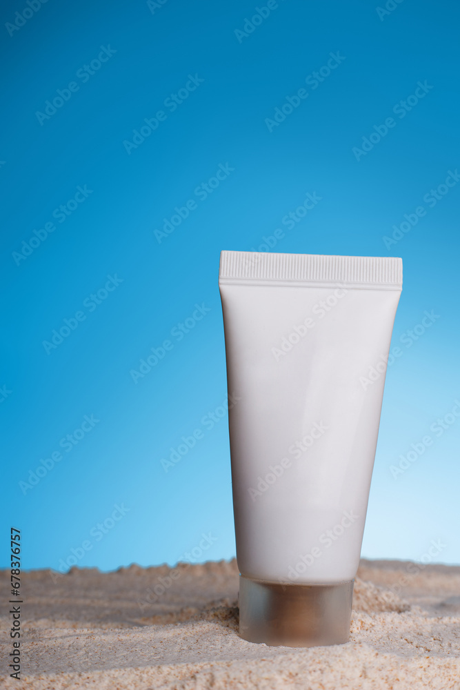 Unbranded body lotion tube with soft liquid. Summer sand backdrop and blue background. Mockup style. Copy space in centre. Skincare and professional cosmetology concept.. Unbranded body lotion tube with soft liquid. Summer sand backdrop and blue background. Mockup style. Copy space in centre. Skincare and professional cosmetology concept..