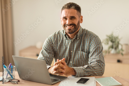 middle aged man smiling as working on laptop in office