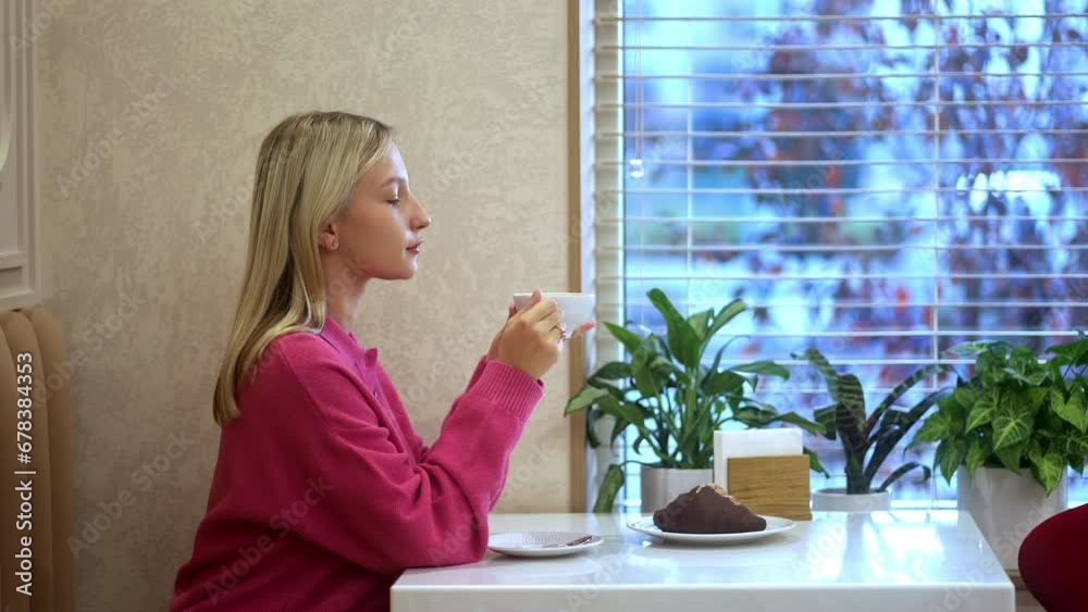 Beautiful girl having breakfast with cappuccino and croissant at a restaurant table near the window. Beautiful flowers on the windowsill. Proper Nutrition and Healthy Eating. Vertical Video Beautiful girl having breakfast with cappuccino and croissant at a restaurant table near the window. Beautiful flowers on the windowsill. Proper Nutrition and Healthy Eating. Vertical Video
