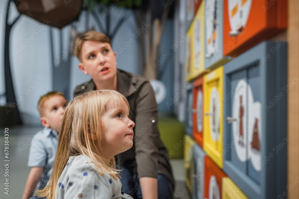 Mother and her two cute little children playing interesting educational interactive games in the natural history museum playroom. Mother and her two cute little children playing interesting educational interactive games in the natural history museum playroom.