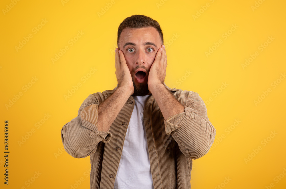 Scared shocked young european man with beard in casual with open mouth put hands to face Scared shocked young european man with beard in casual with open mouth put hands to face