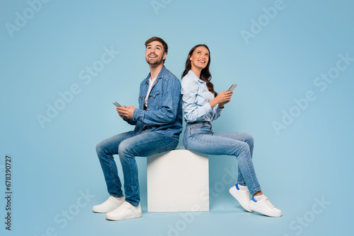 Spouses with mobiles gaze up, blue background photo