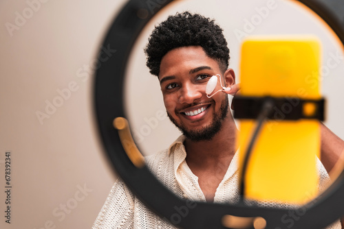 Young latin man using facial roller in makeup setup photo