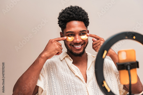 Young latin man applying skincare with face patch in front of ring light photo
