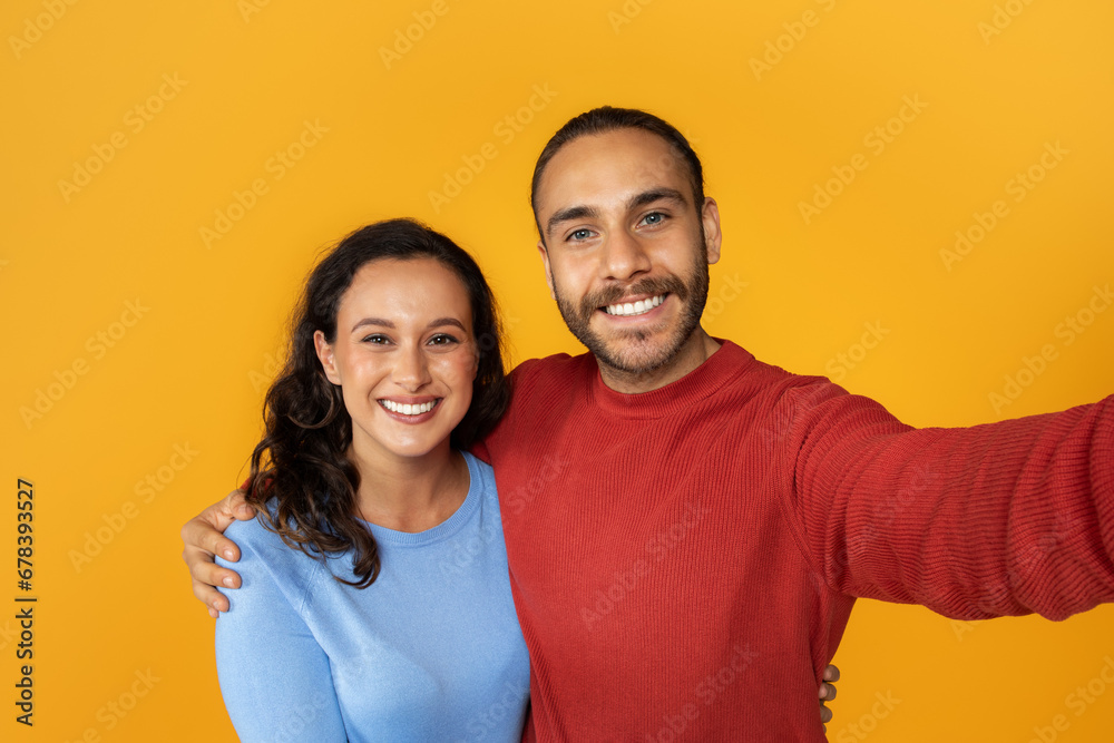 Cute positive young couple taking selfie on yellow background Cute positive young couple taking selfie on yellow background