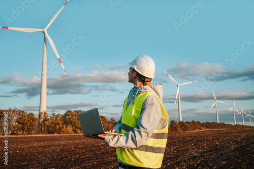 Engineer with laptop at wind farm during sunset photo