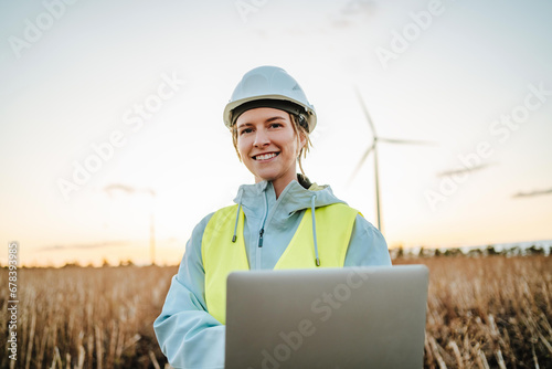 Smiling engineer with laptop near wind turbines at dusk photo