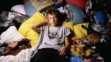 Young man lying on his belongings in his messy room.