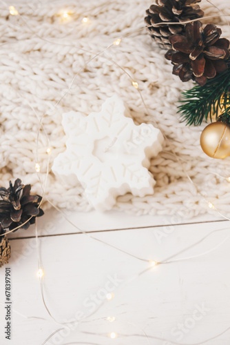 Cozy candle as snowflake with Christmas decoration on the white and knitted background. New year or Christmas holiday concept, holidays card.