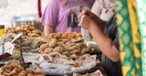 Fototapeta Naklejka Na Ścianę i Meble -  Close-up of a woman at her street food stall in a medieval market filled with trays of handmade products and small cakes and sweets.