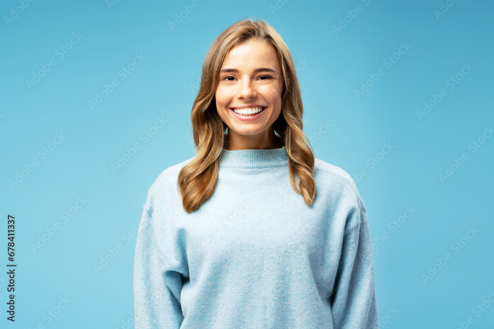Smiling attractive woman with silky wavy hair wearing cozy sweater looking at camera standing isolated on blue background. Concept of beauty, hair care, makeup Smiling attractive woman with silky wavy hair wearing cozy sweater looking at camera standing isolated on blue background. Concept of beauty, hair care, makeup
