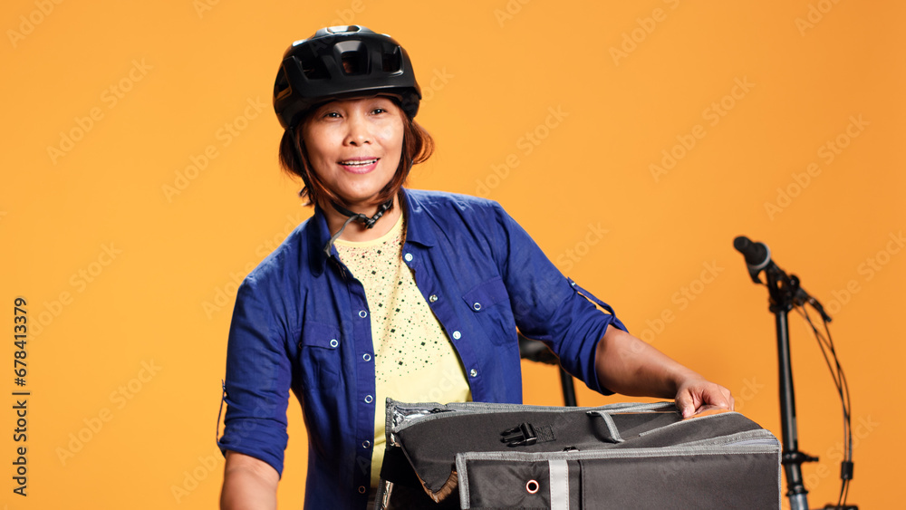 Happy pizza delivery woman wearing bicycle equipment bringing order to client. Close up of cheerful BIPOC courier getting meal boxes out of thermal food bag, isolated over studio background Happy pizza delivery woman wearing bicycle equipment bringing order to client. Close up of cheerful BIPOC courier getting meal boxes out of thermal food bag, isolated over studio background