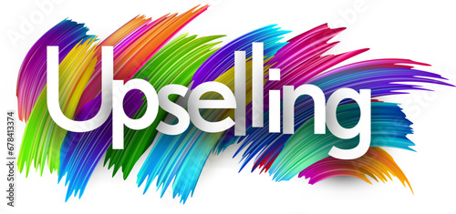 Upselling paper word sign with colorful spectrum paint brush strokes over white.