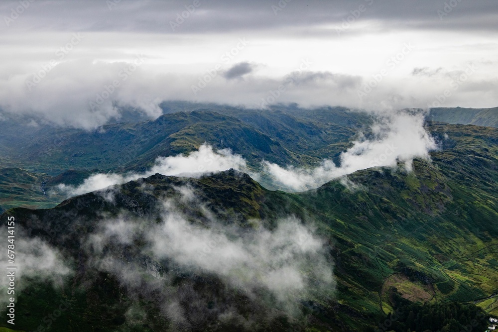 Aerial shot of a field of high mountains touching the clouds in the sky