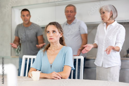 Domestic quarrel - offended young woman sits at the table while parents and young husband yell at her