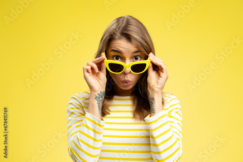 Portrait of excited beautiful woman wearing yellow sunglasses looking at camera standing isolated on yellow background. Summer concept