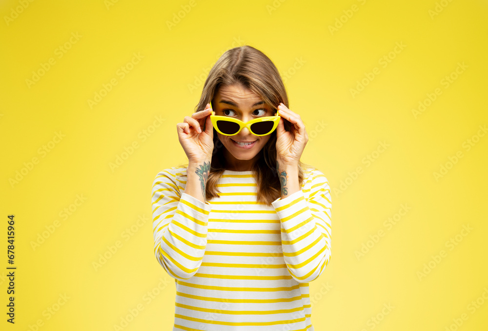 Portrait of smiling attractive woman wearing yellow sunglasses looking away, standing isolated on yellow background. Summer concept Portrait of smiling attractive woman wearing yellow sunglasses looking away, standing isolated on yellow background. Summer concept