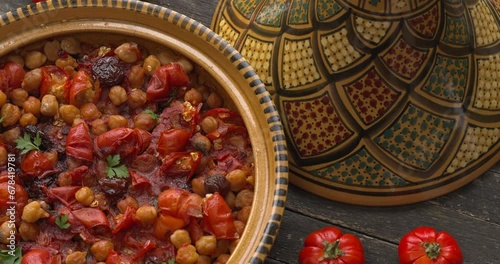 Moroccan vegan tagine made of Ethiopian eggplant and chickpea in an open traditional tagine pot. A few Ethiopian eggplants next to it. Top view, table spin.