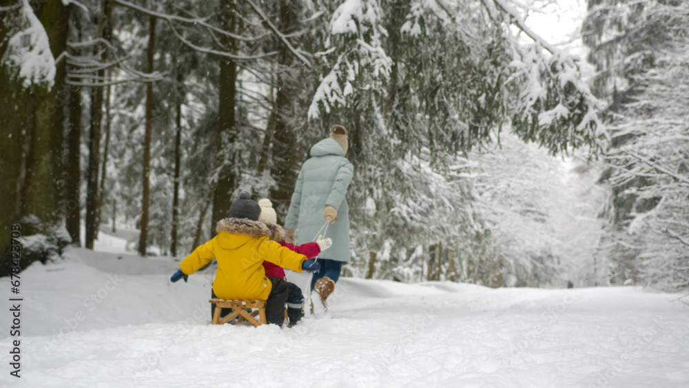 Adult mother rides children with excited expression on big sled in snowy forest