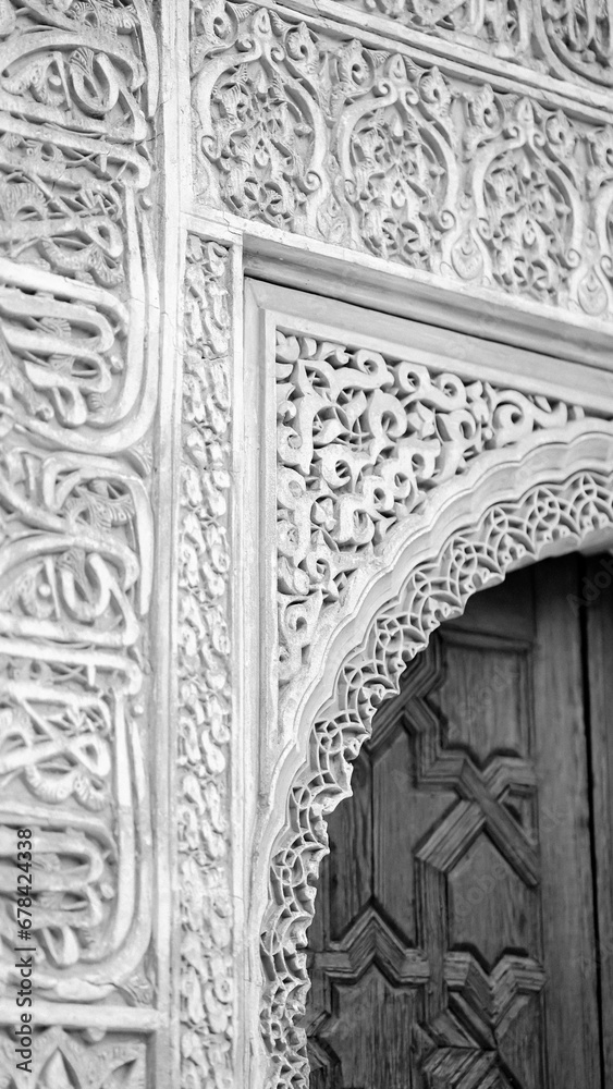 Vertical grayscale shot of Islamic architecture with quranic inscriptions on Alhambra Castle
