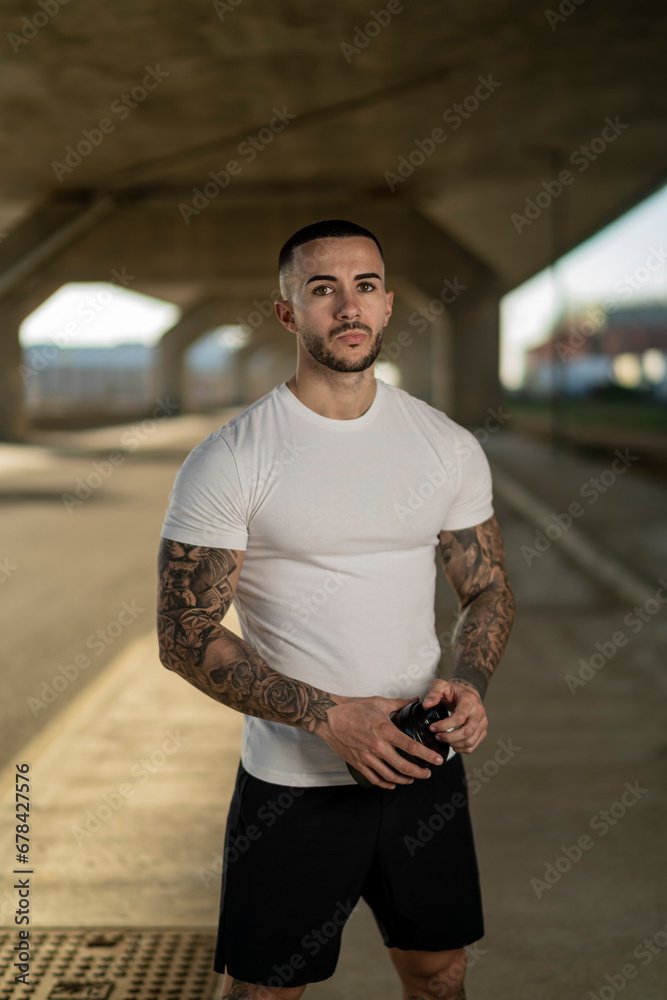 Fototapeta premium Chico joven musculoso y tatuado haciendo ejercicio y usando smartphone en carretera
