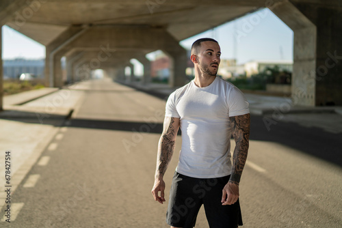 Chico joven musculoso y tatuado haciendo ejercicio y usando smartphone en carretera
