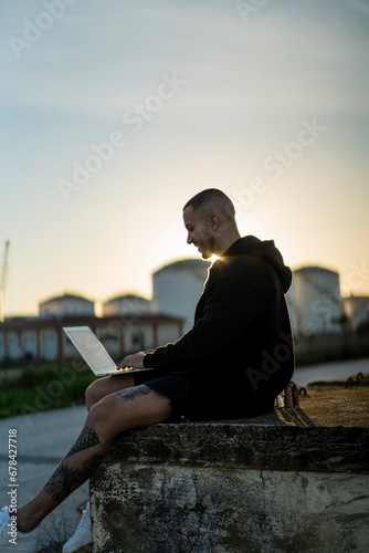 Chico joven emprendedor trabajando en su laptop al atardecer con un puente de fondo 
