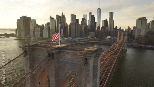 Aerial shot of The American Flag flying high above New York City's Brooklyn Bridge at sunset.