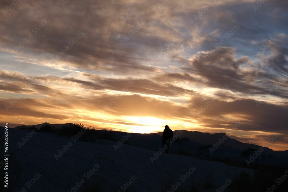 Scenic view of a person in the snowy field watching the mesmerizing sunset in the cloudy sky
