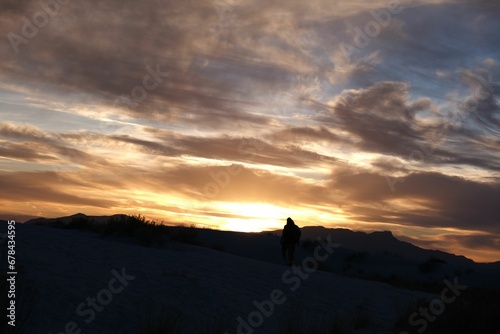 Scenic view of a person in the snowy field watching the mesmerizing sunset in the cloudy sky