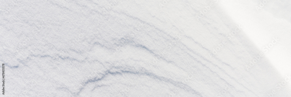 Fototapeta premium Beautiful winter background with snowy ground. Natural snow texture. Wind sculpted patterns on snow surface. Wide panoramic texture for background and design. Closeup top view with copy space.