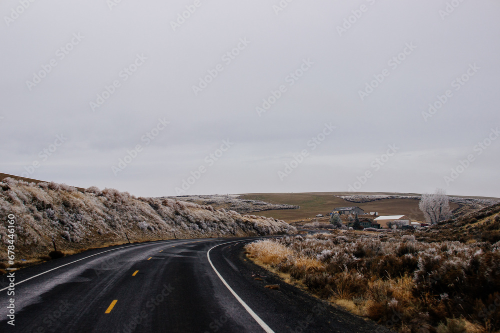 Asphalt Road in the middle of a mountainous area covered with frost, with cozy houses on a winter cloudy day. American landscape