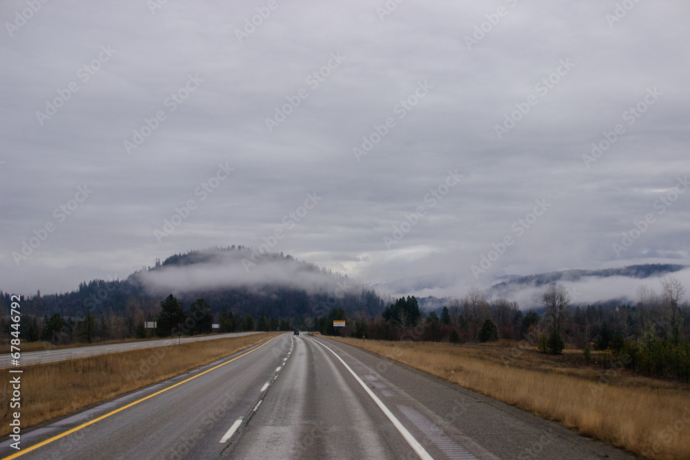 Asphalt road in the middle of high mountains, covered with fog and clouds, at dusk. American winter landscape of a mountainous area covered with fir forest Asphalt road in the middle of high mountains, covered with fog and clouds, at dusk. American winter landscape of a mountainous area covered with fir forest