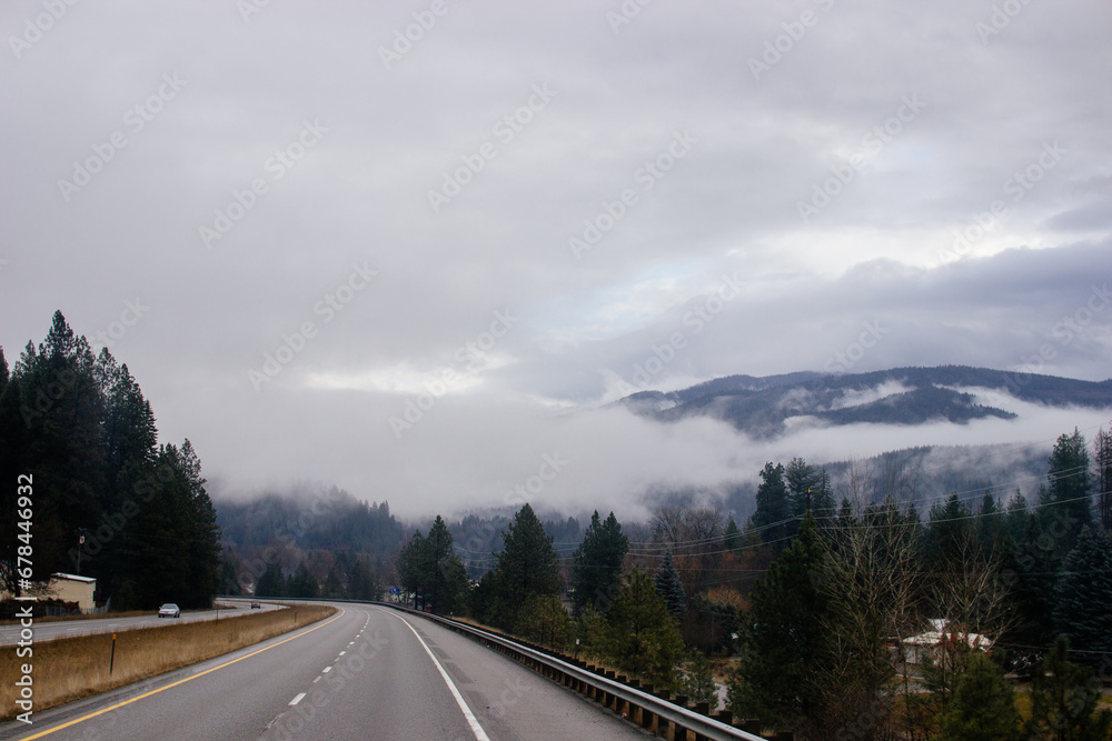 Asphalt road in the middle of high mountains, covered with fog and clouds, at dusk. American winter landscape of a mountainous area covered with fir forest Asphalt road in the middle of high mountains, covered with fog and clouds, at dusk. American winter landscape of a mountainous area covered with fir forest