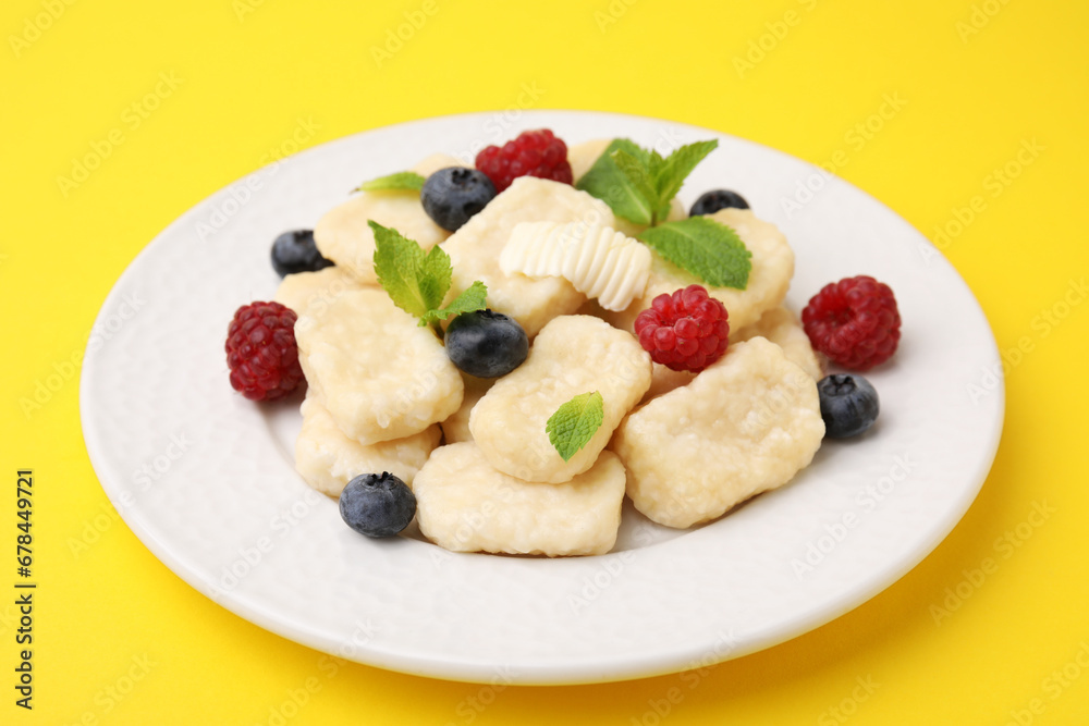 Plate of tasty lazy dumplings with berries, butter and mint leaves on yellow background Plate of tasty lazy dumplings with berries, butter and mint leaves on yellow background
