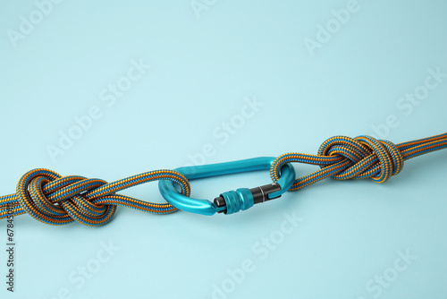 One metal carabiner with ropes on light blue background, space for text