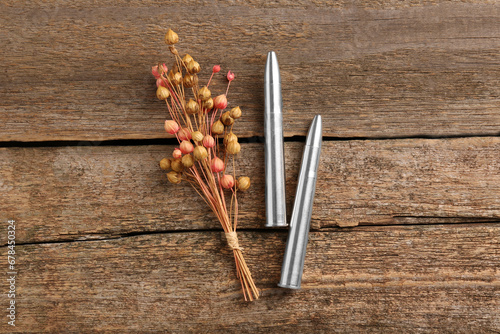 Metal bullets and beautiful dry plant on wooden table, flat lay