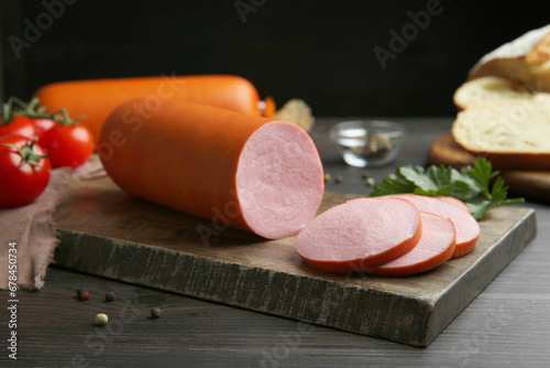 Board with tasty boiled sausage on dark wooden table, closeup