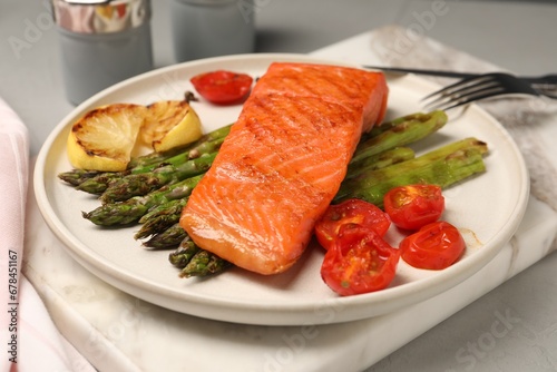 Tasty grilled salmon with asparagus, tomatoes and lemon on light grey table, closeup