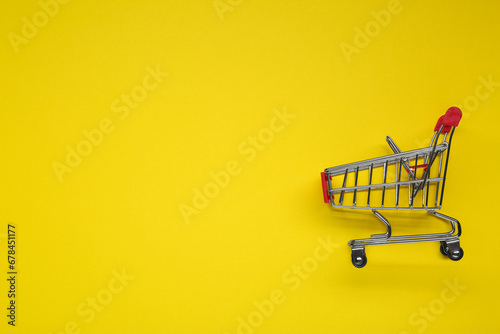 Small metal shopping cart on yellow background, top view. Space for text