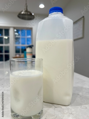 Half gallon of low-fat milk on the counter next to a full glass