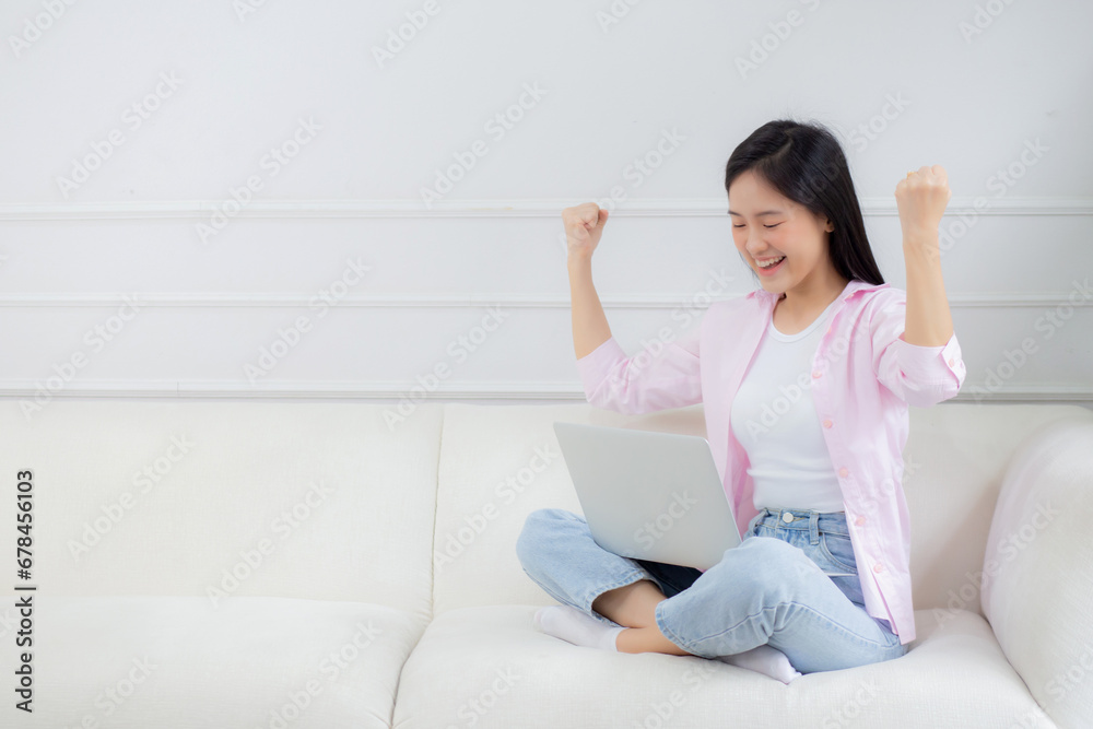 Happiness young asian woman sitting on sofa and working on laptop computer while successful and excitement at home, freelance female using notebook and achievement, business and lifestyles concept. Happiness young asian woman sitting on sofa and working on laptop computer while successful and excitement at home, freelance female using notebook and achievement, business and lifestyles concept.