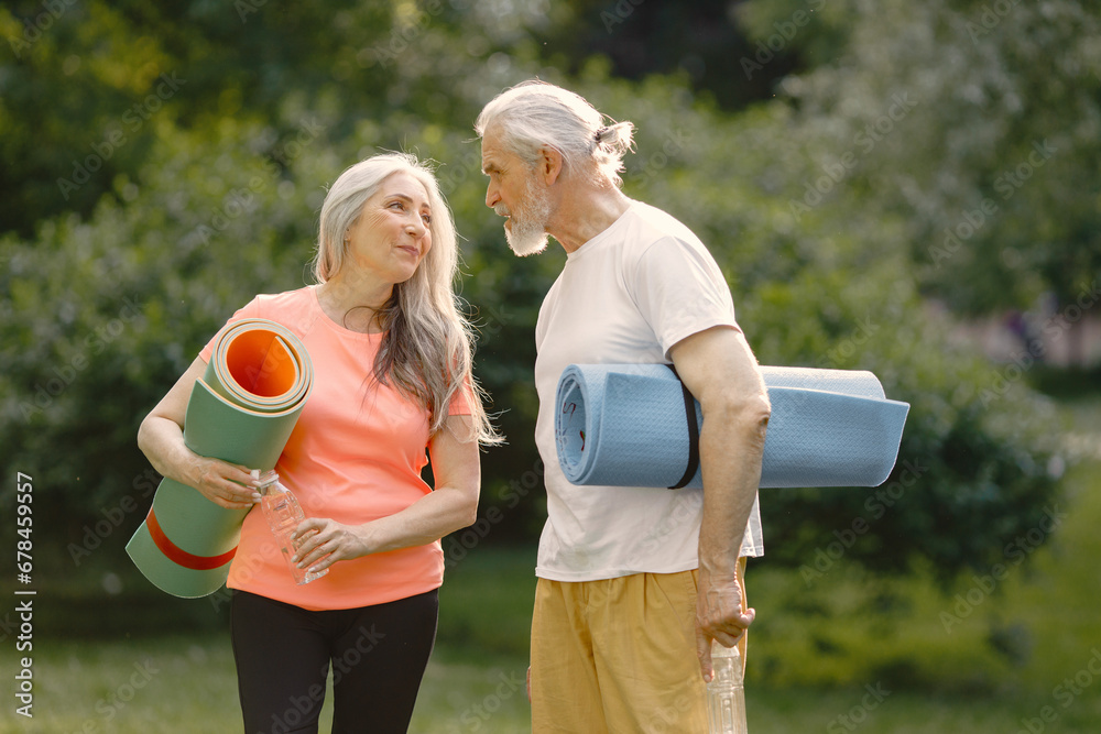Senior couple with exercise mats standing at park and talking Senior couple with exercise mats standing at park and talking