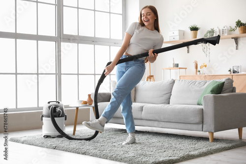 Young woman with vacuum cleaner singing at home photo