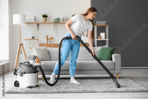 Young woman vacuuming carpet at home photo