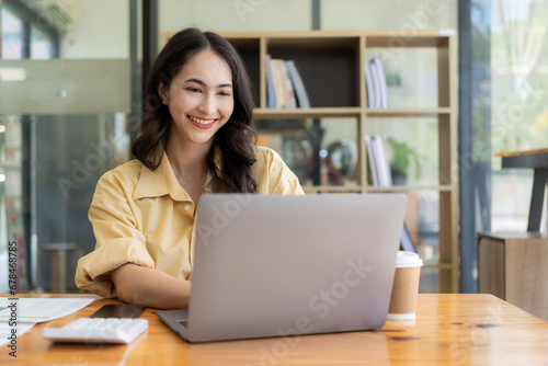 Ambitious Asian girl working from home Looking at laptop screen and financial documents, woman is checking email or doing research while working remotely.