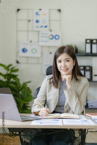 Ambitious Asian girl working from home Looking at laptop screen and financial documents, woman is checking email or doing research while working remotely.