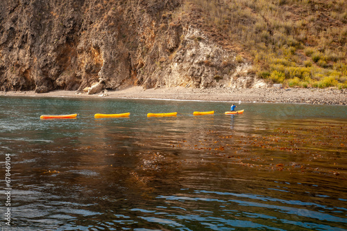 A man paddeling a group of yellow kyaks in a row toward a beach photo