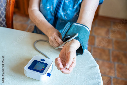 Senior woman start to check blood pressure level at home, older female suffering from high blood pressure sitting and using a pulsometer, tonometer photo