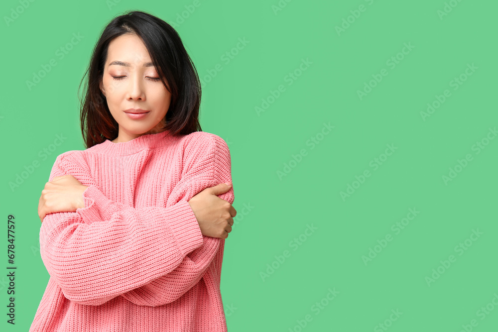 Fototapeta premium Young Asian woman hugging herself on green background